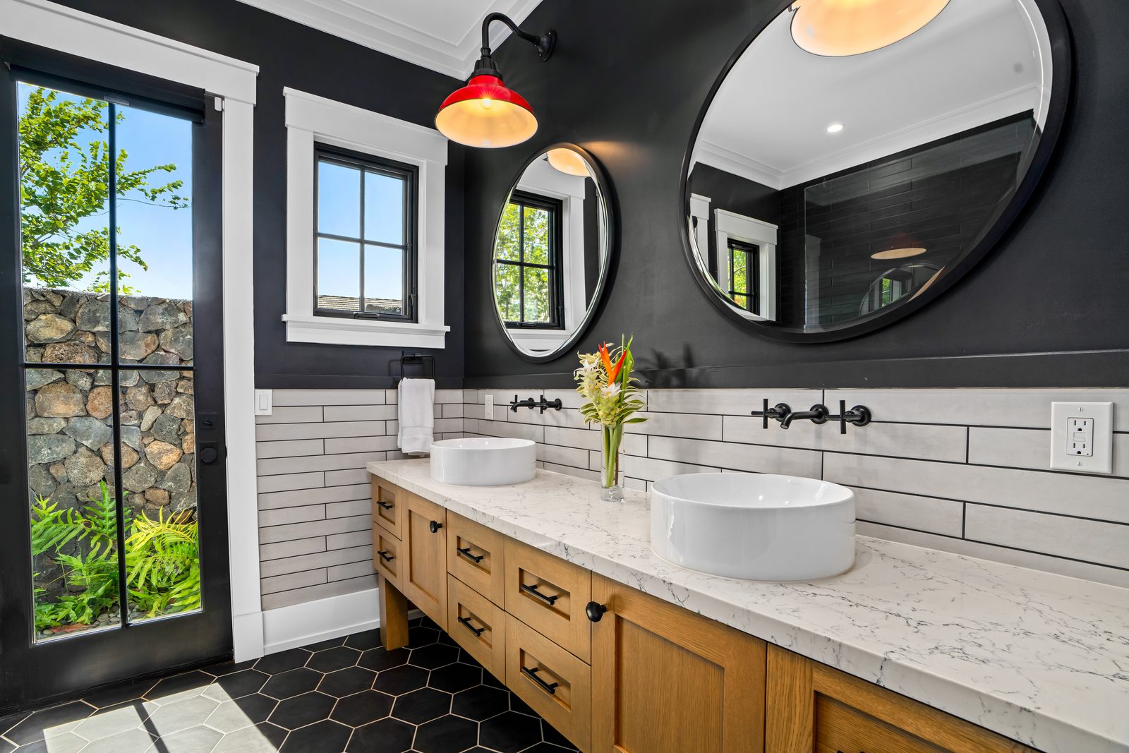 Red Room bathroom with a wood double vanity, round mirrors and a glass door to the outdoor shower