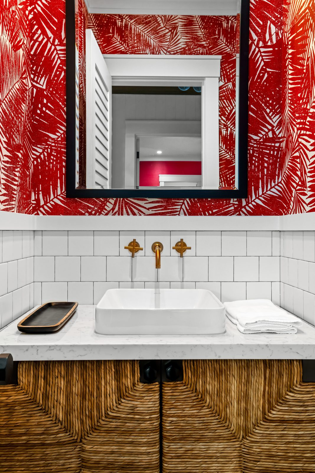 The powder room with red palm-print wallpaper and a woven vanity